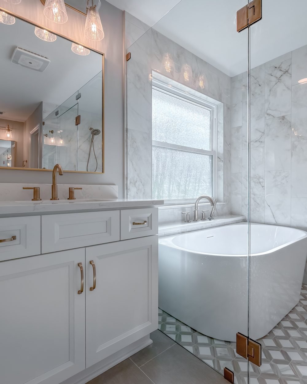 Primary bathroom with a freestanding soaking tub beneath a window and marble-veined large-format tile. One of our renovation projects, Tallahassee FL.