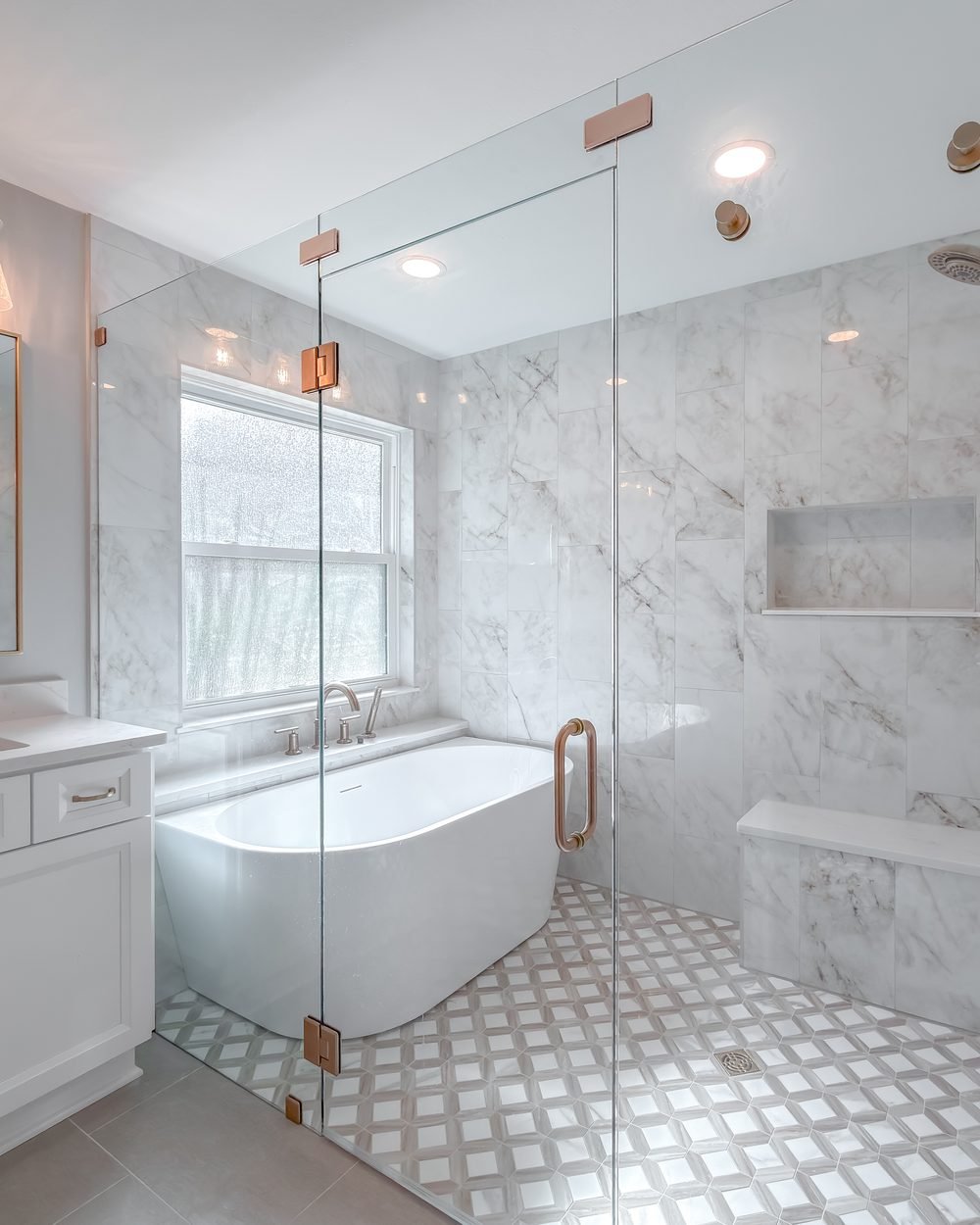 Primary bathroom with a freestanding tub, sage double vanity and frameless glass shower in marble-veined tile. Tallahassee, FL