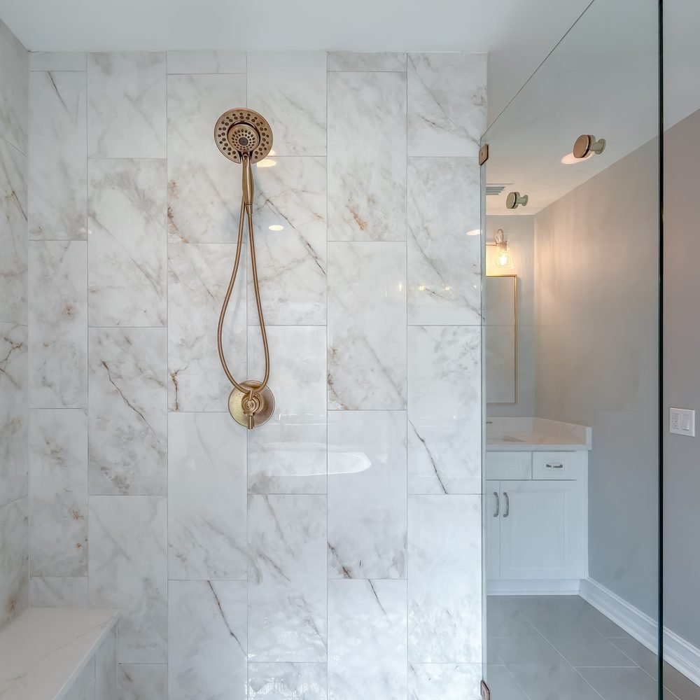 Brass handheld shower fitting on a slide bar against a marble-veined wall