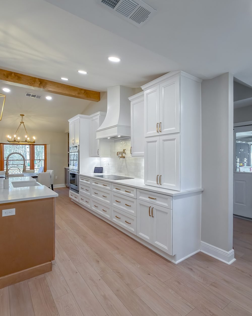 Open kitchen with a white range hood, exposed beam and brass ring chandelier over a wood island. Whole home renovations Tallahassee, FL.
