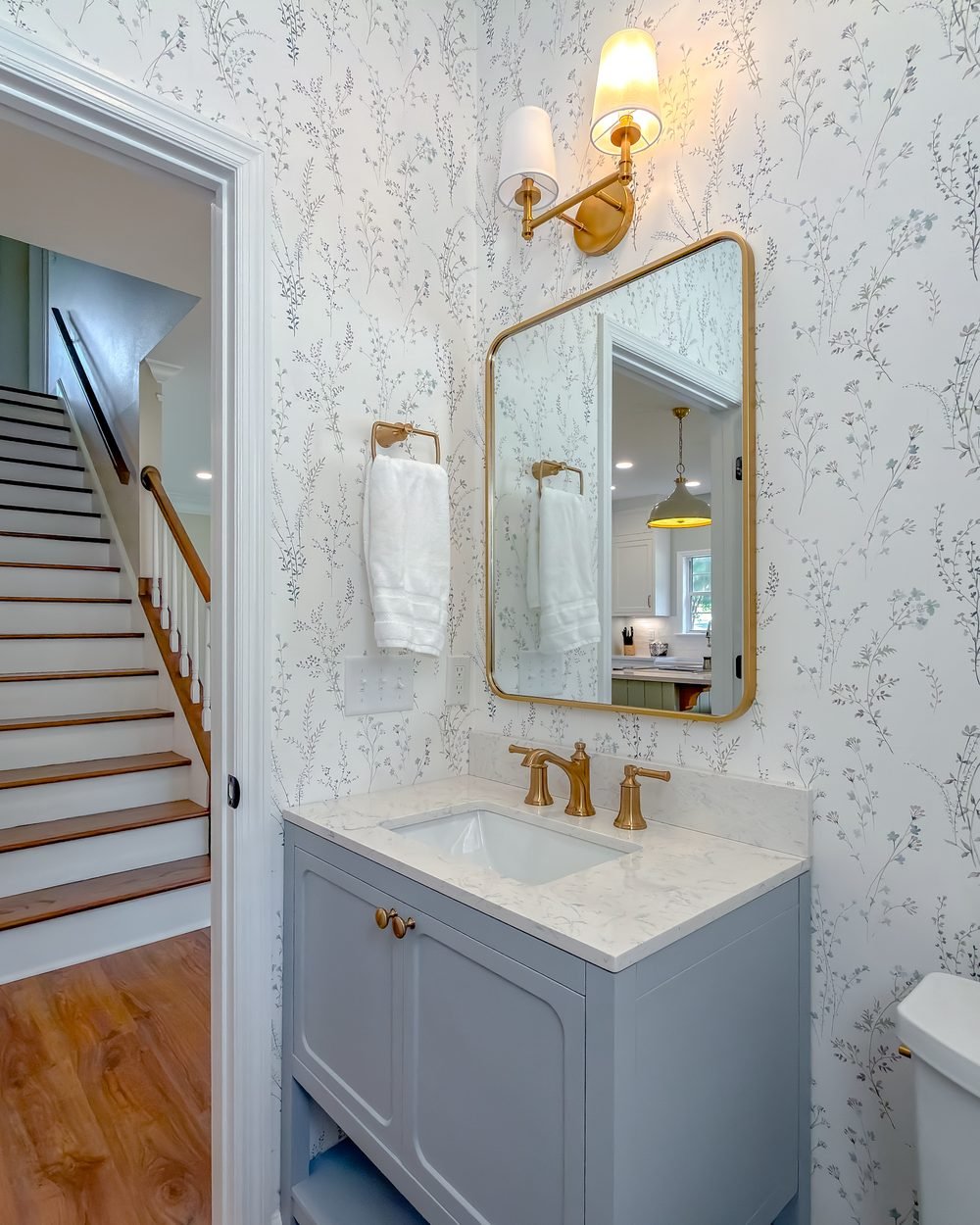 Powder room with a pale blue vanity, brass mirror and patterned wallpaper. Tallahassee, FL