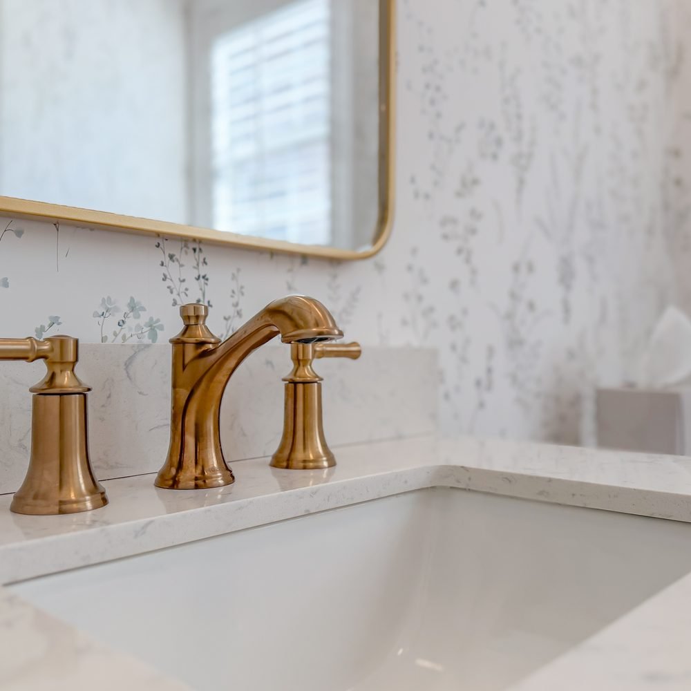 Brass faucet on a marble vanity top with a beaded mirror above