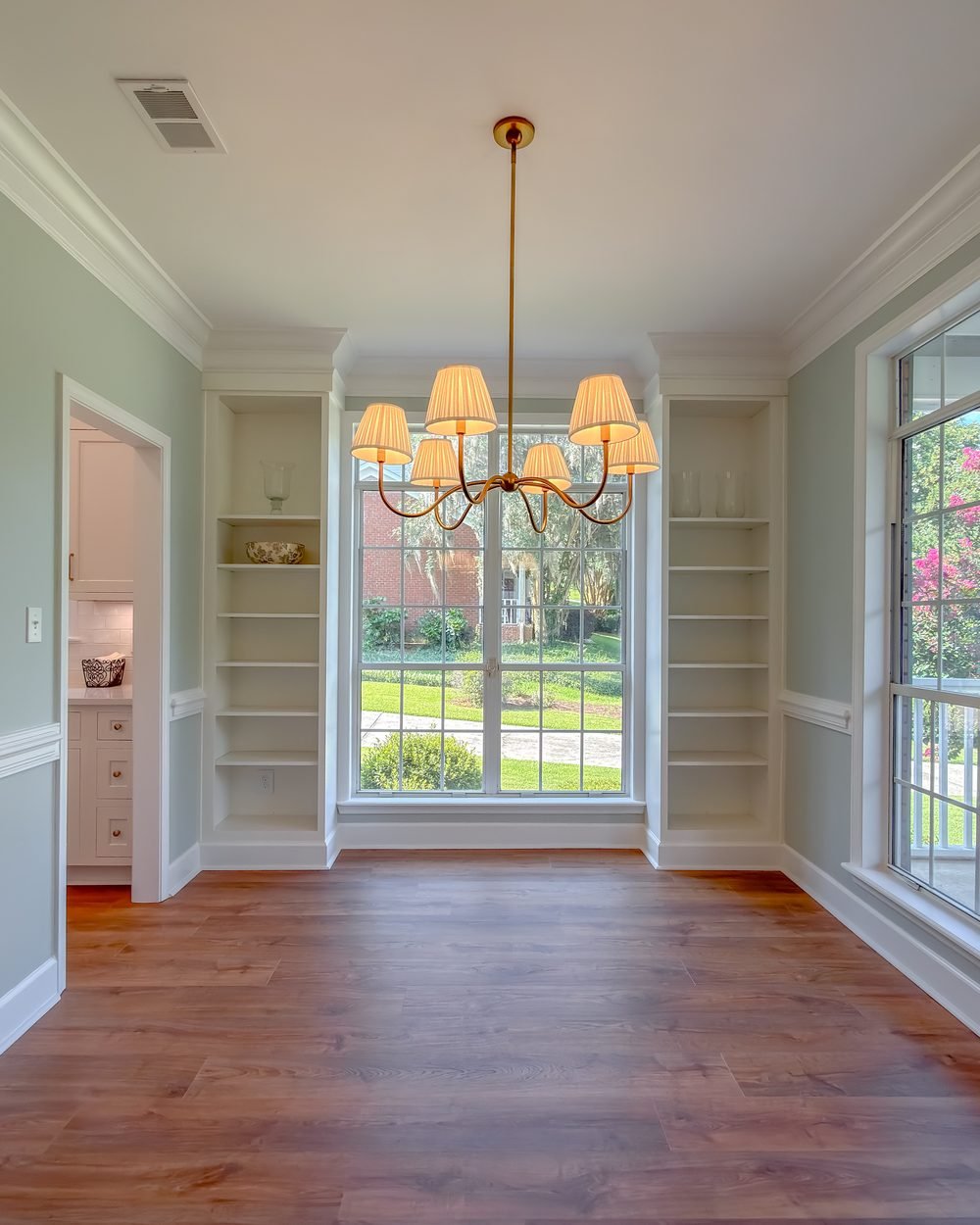 Formal dining room with wainscoting, a brass chandelier and a wall of windows. Interior renovation in Tallahassee, FL