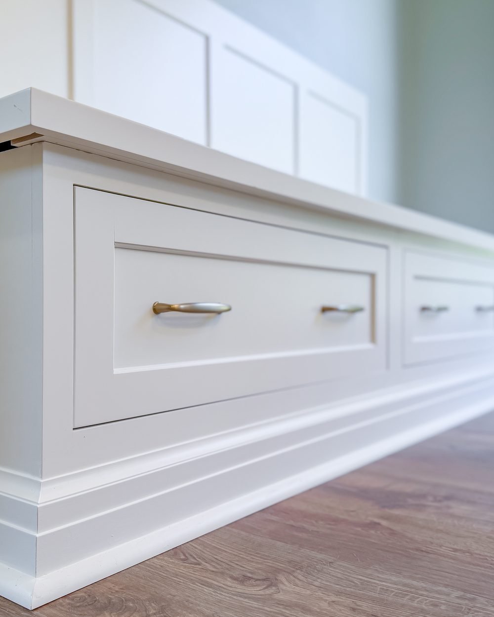 Custom-built window seat with deep storage drawers, brass pulls and a paneled back, finished in white against a pale sage wall. Interior renovation by Pristine Renovations in Tallahassee, FL