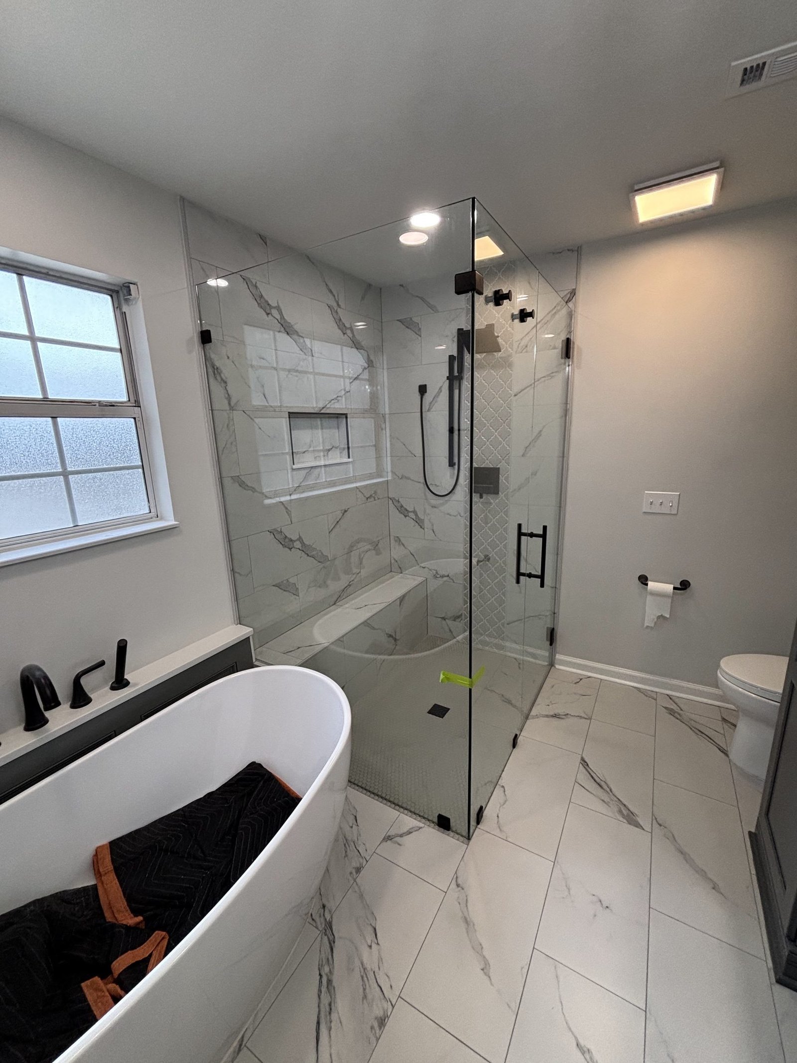 A freestanding soaking tub beside a frameless glass shower with marble-look large-format tile, Tallahassee, FL