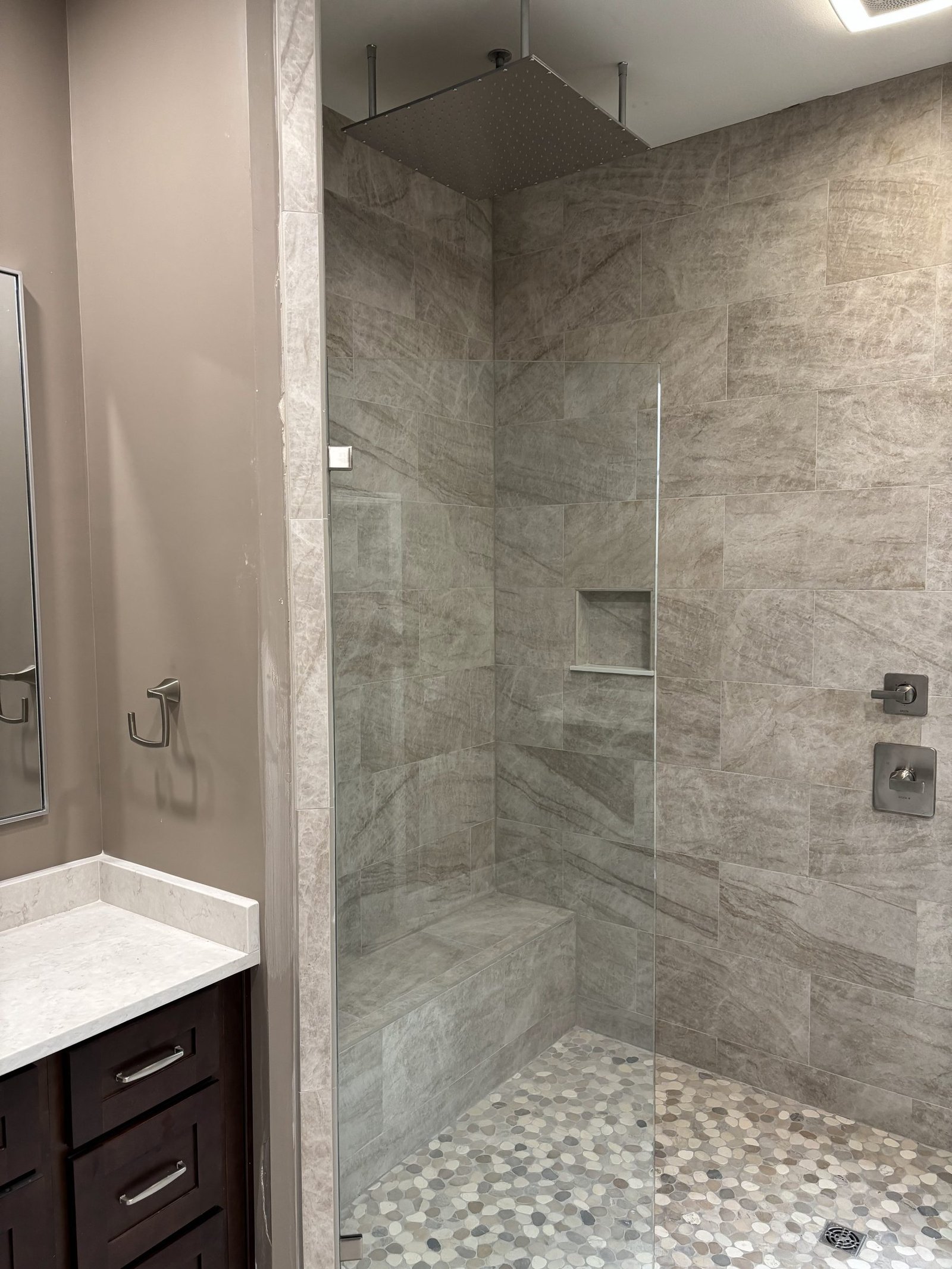 Walk-in shower in large-format stone tile with a pebble floor and a recessed niche. Tallahassee, Florida.