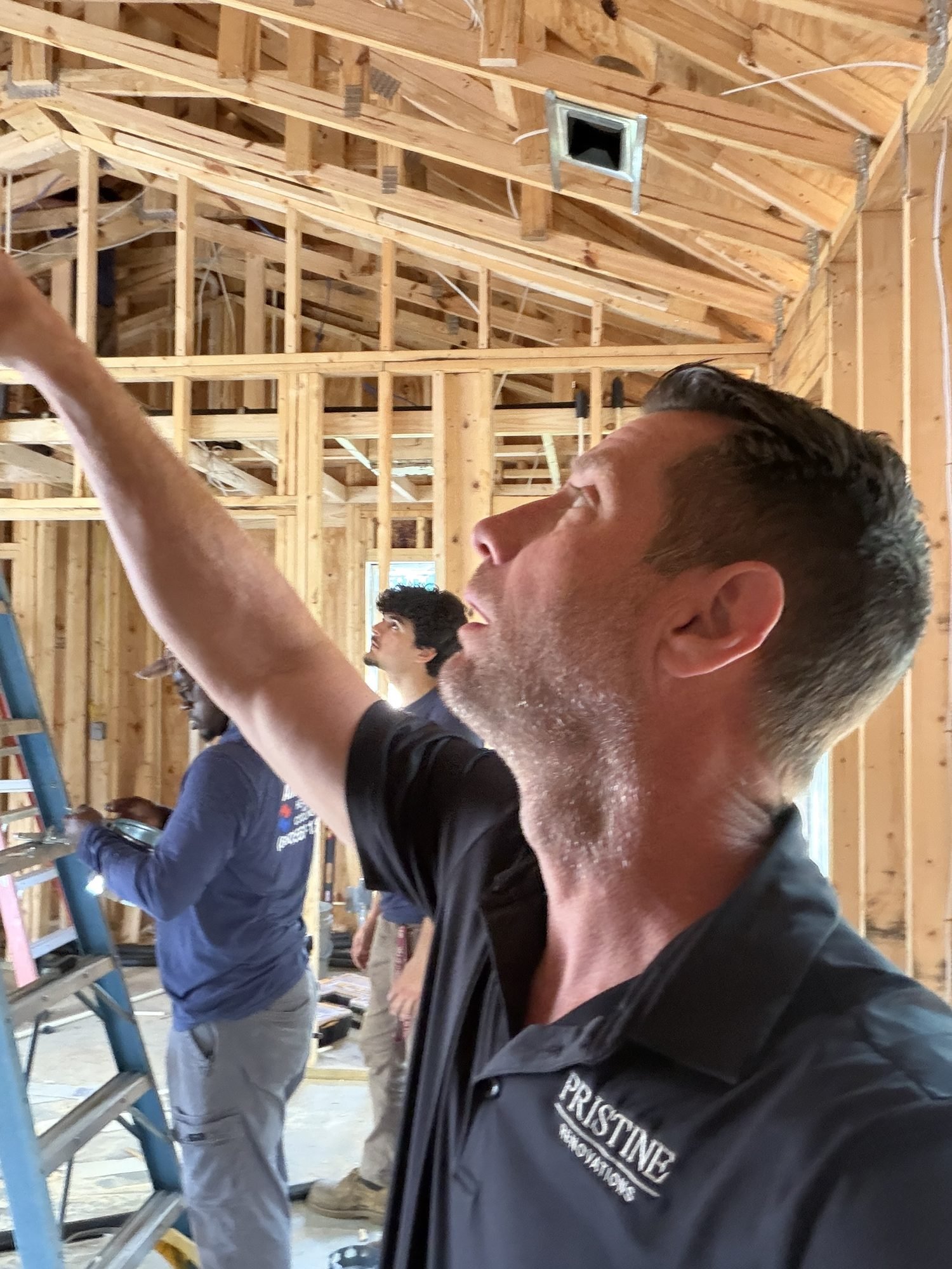 A Pristine Renovations superintendent in a branded polo inspecting newly exposed roof framing during a renovation in Tallahassee, FL