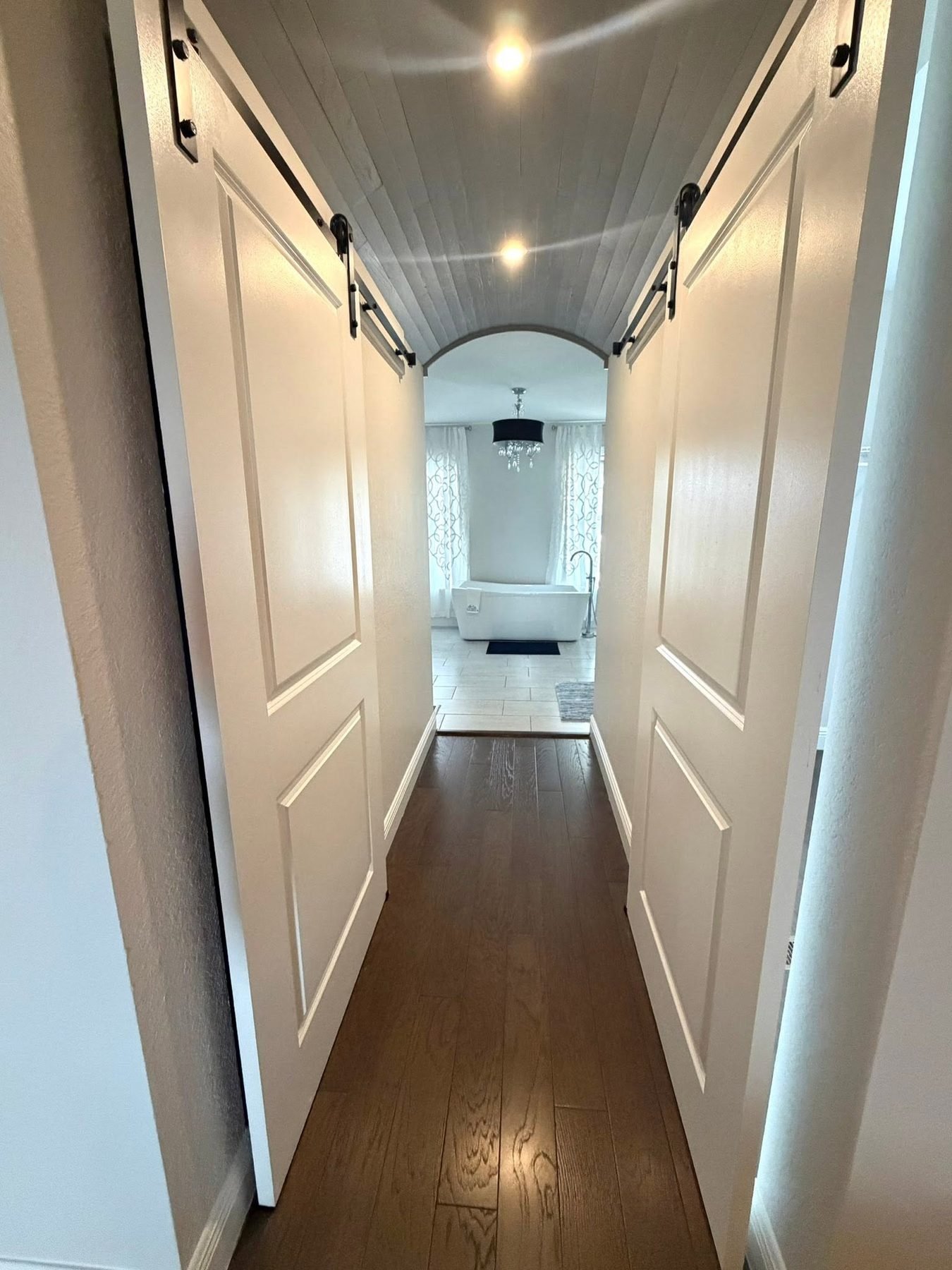 A hallway with sliding barn doors and a shiplap ceiling connecting two areas of a renovated home, Tallahassee, FL