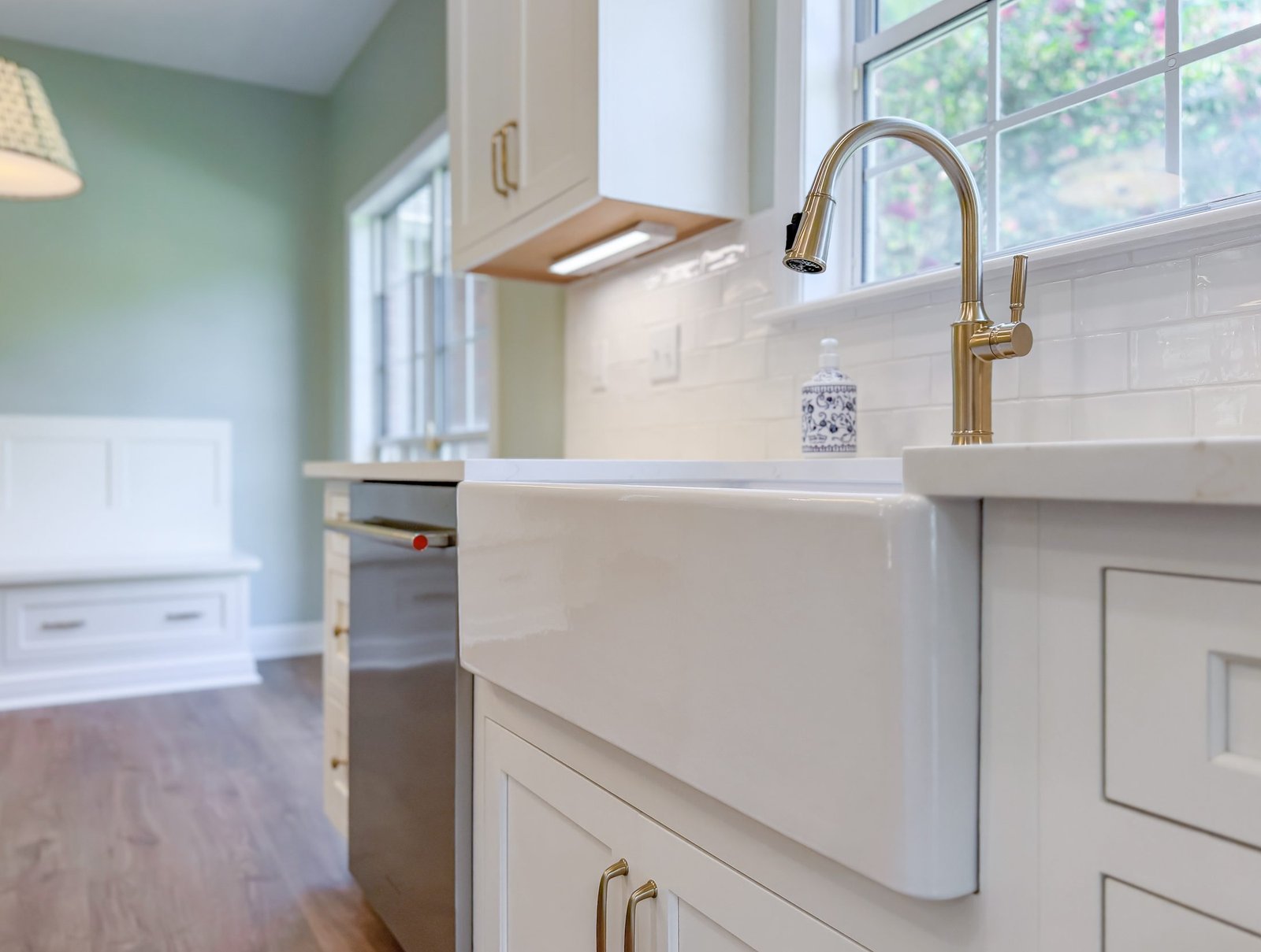 Farmhouse apron sink with a brass gooseneck faucet set beneath a window in a renovated white kitchen, Tallahassee, FL