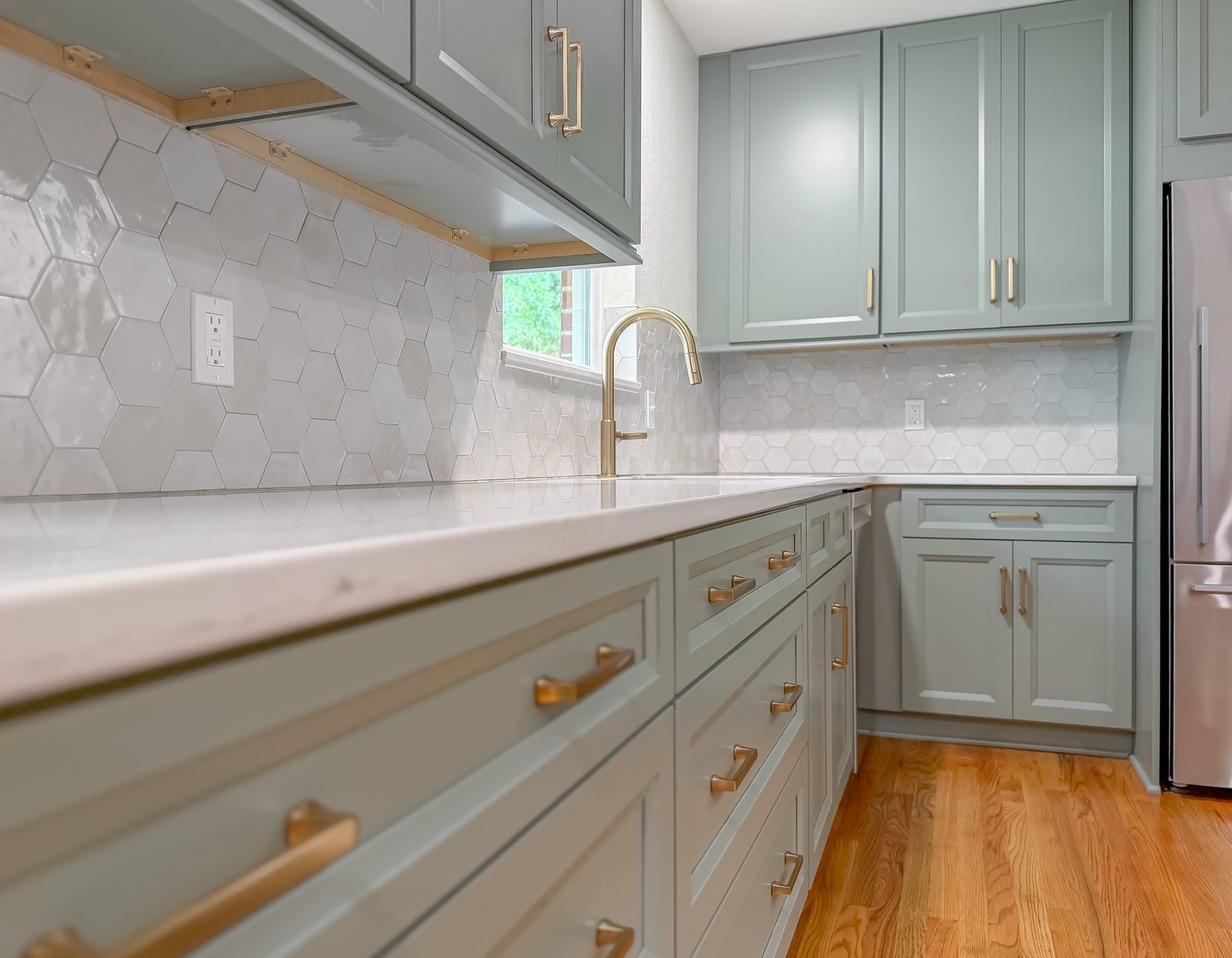 Detail of sage green kitchen cabinetry with aged brass pulls, a quartz countertop and a hexagonal tile backsplash, Tallahassee, FL