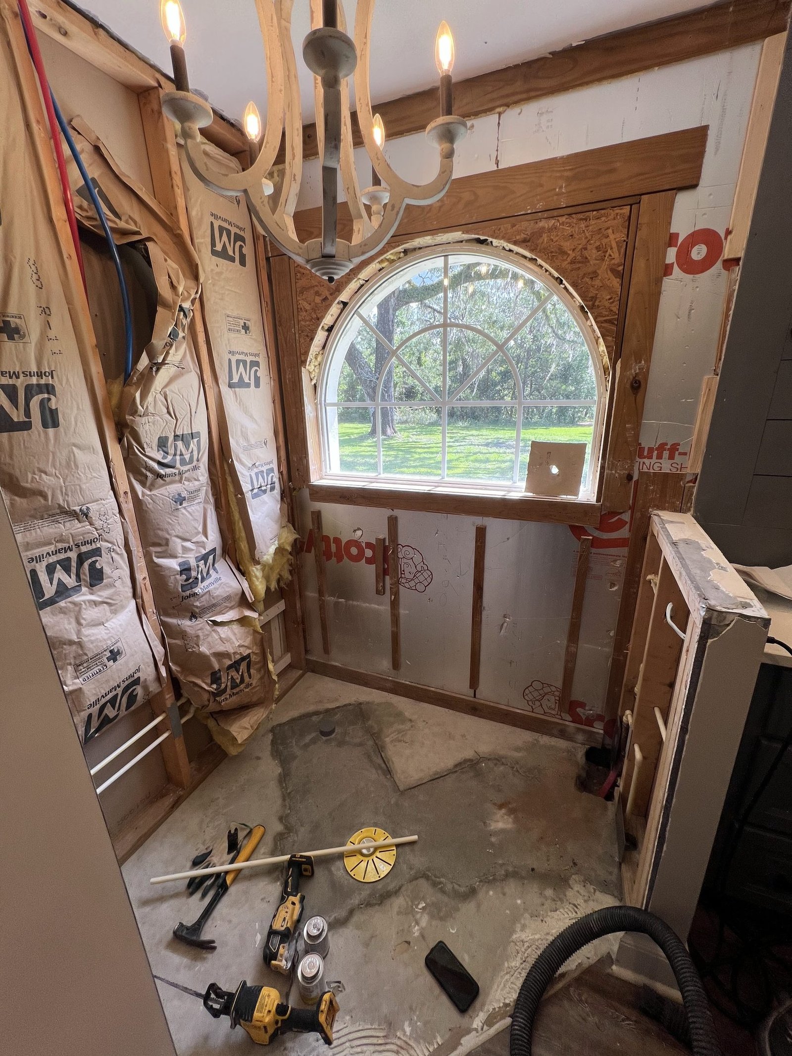 A primary bathroom taken back to the studs around an original arched window, with tools on the subfloor, Tallahassee, FL