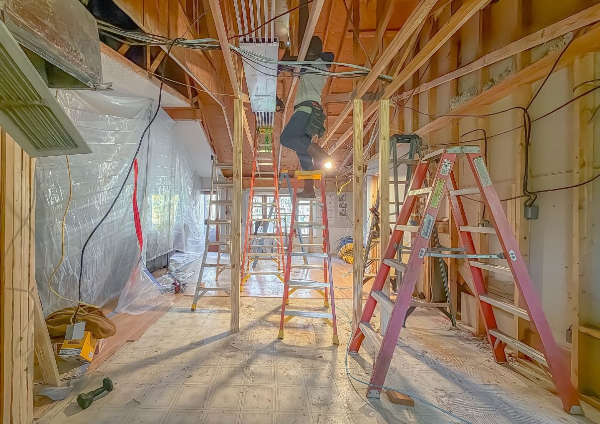 Framing work underway with ladders and protective sheeting through an open interior. Tallahassee, Florida.