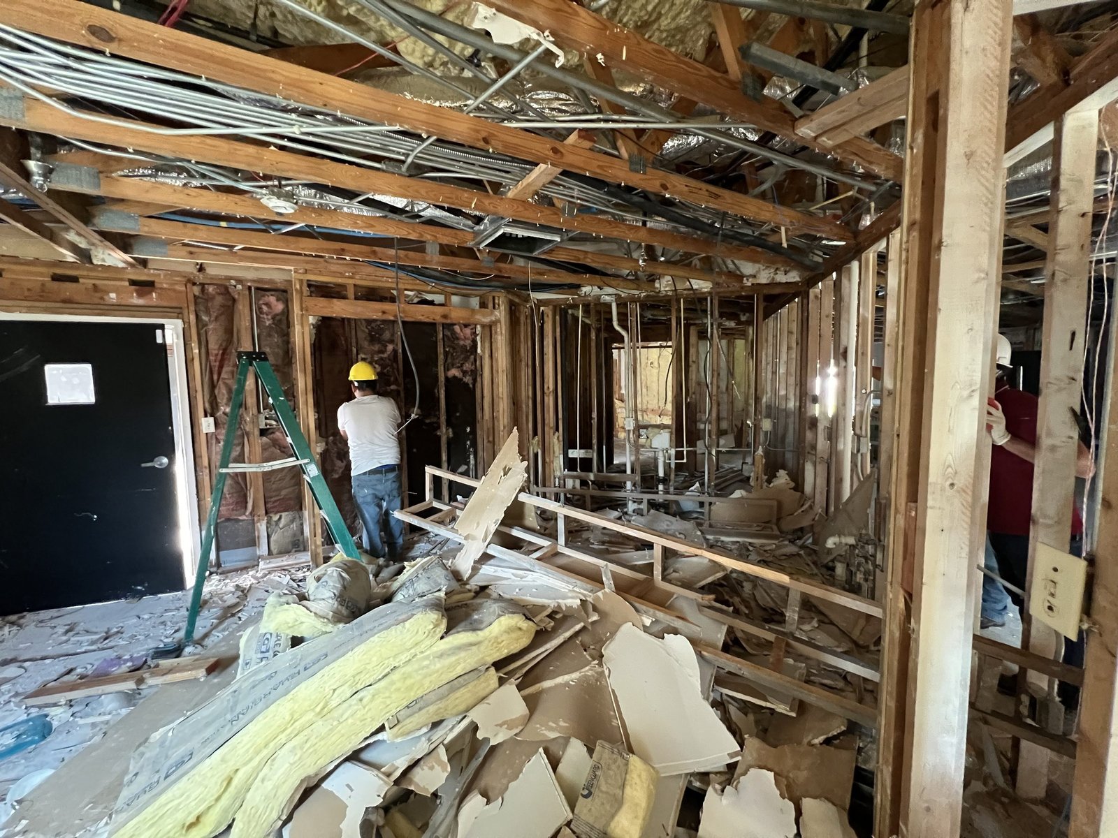 A house stripped back to its framing and joists mid-renovation, with a crew member in a hard hat working among the debris, Tallahassee, FL