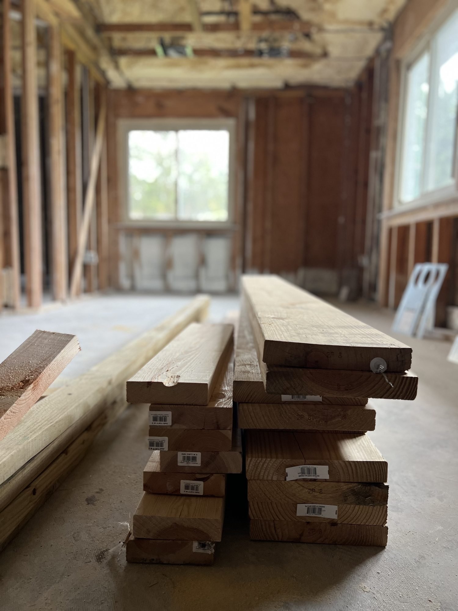 Stacked structural lumber and beams on a bare subfloor inside a room stripped to the studs, Tallahassee, FL