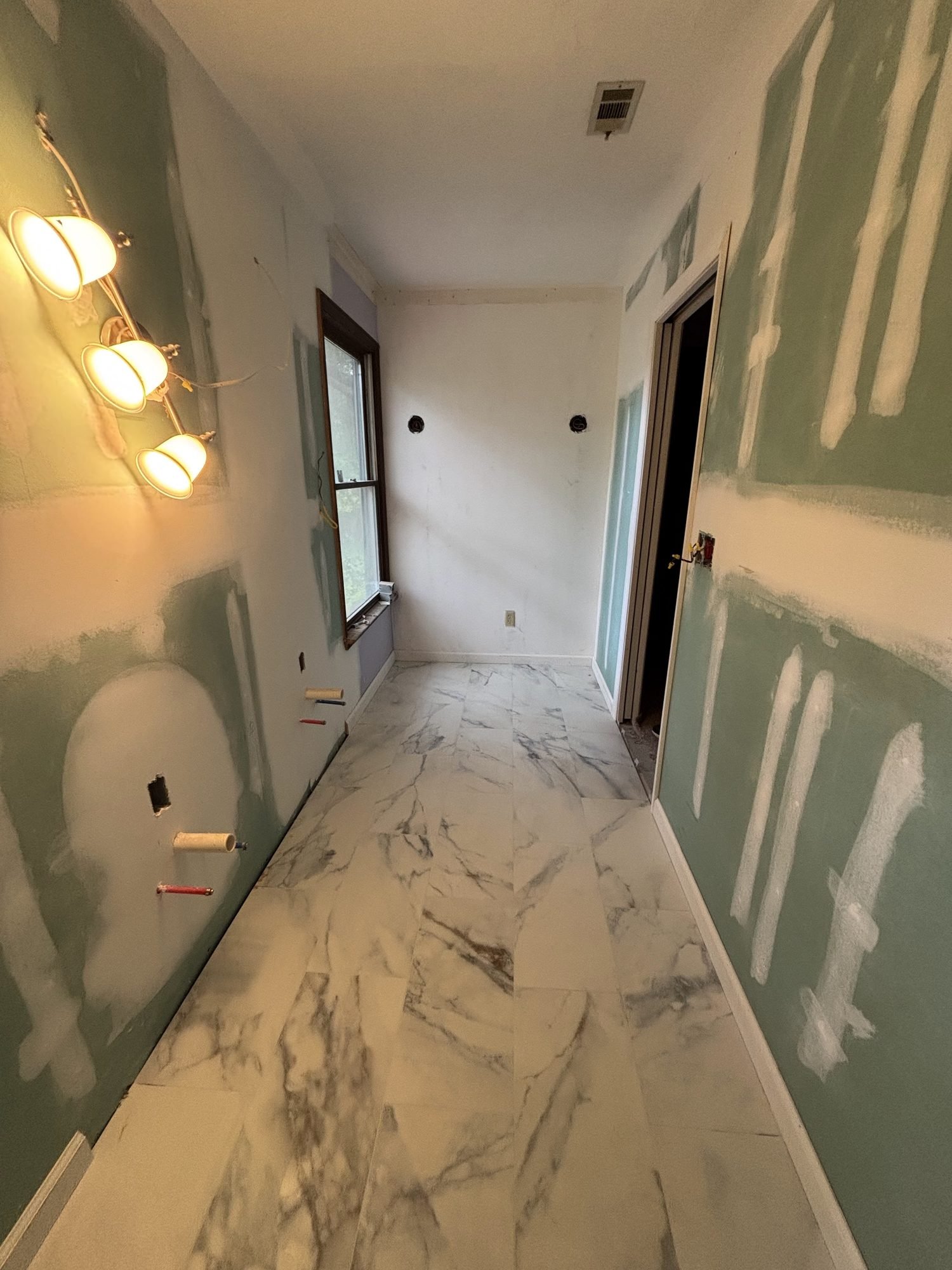 Large-format marble-look floor tile being laid along a finished hallway, Tallahassee, FL