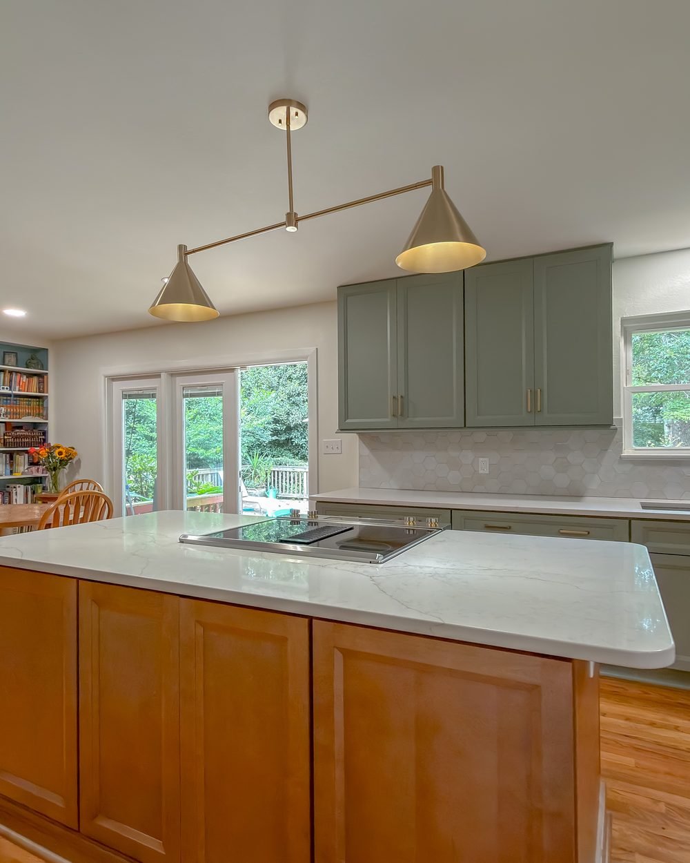 Kitchen with soft sage cabinetry, a quartz island, brass pendants and a wall of bookshelves. Kitchen remodel in Tallahassee, FL