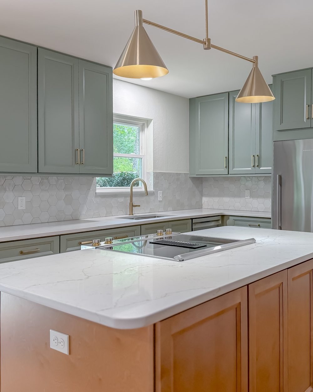 Renovated kitchen with a sage island, induction cooktop, brass pendants and open sightlines to the dining area. Tallahassee, FL