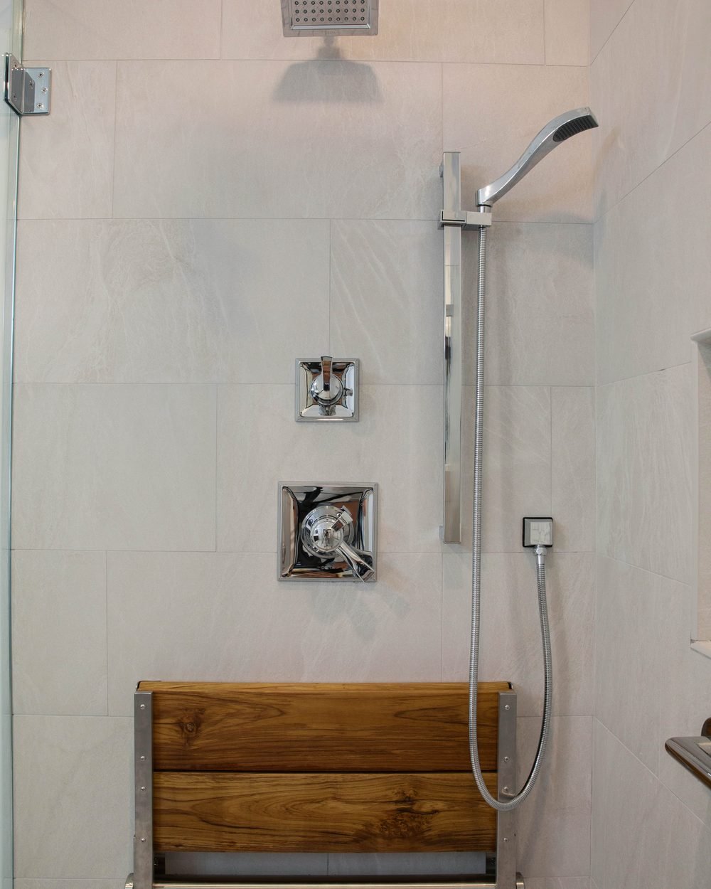 Walk-in shower with a teak bench, handheld shower on a slide bar and a polished support rail set into large-format tile. Tallahassee, FL
