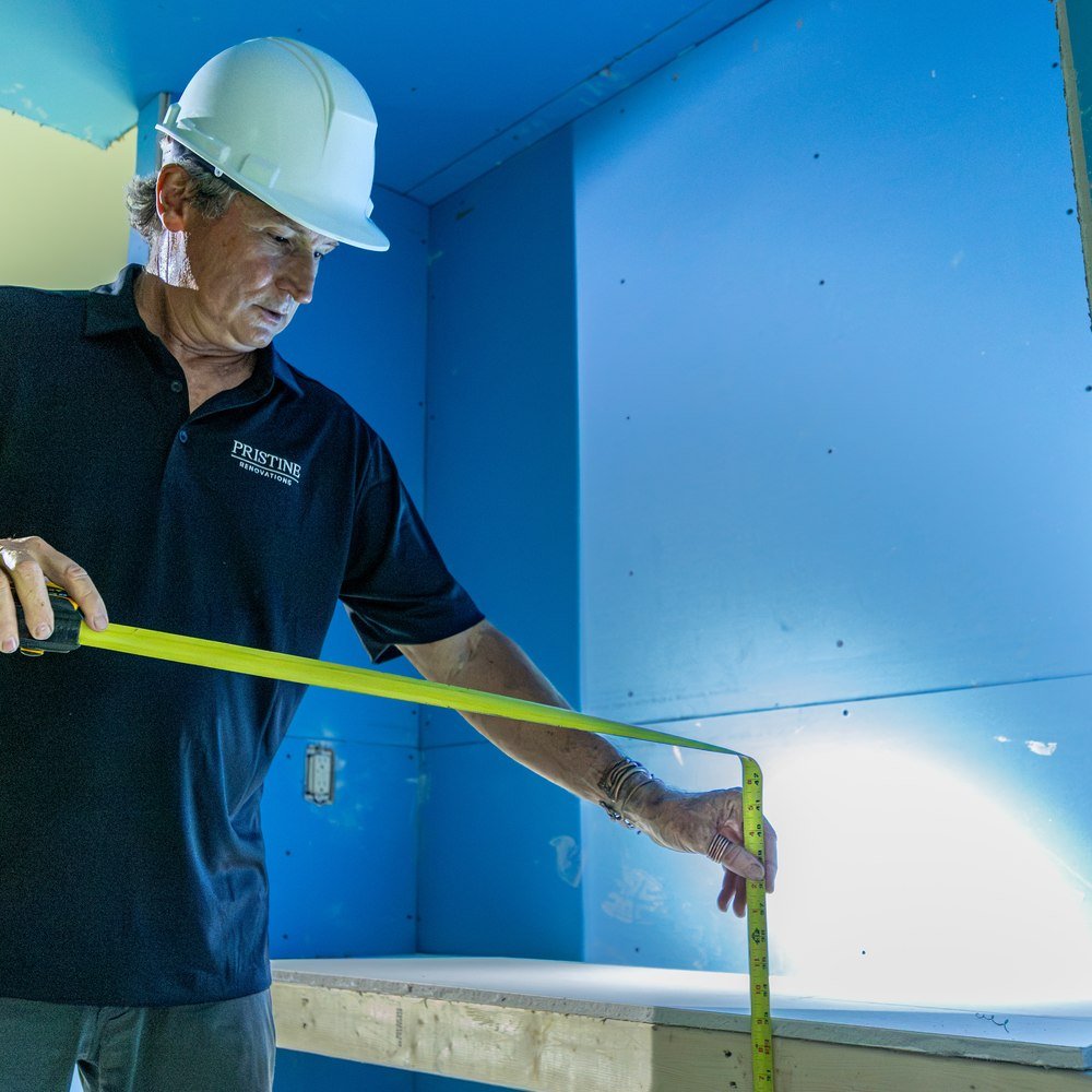 Pristine worker measuring a bathroom wall opening during renovation
