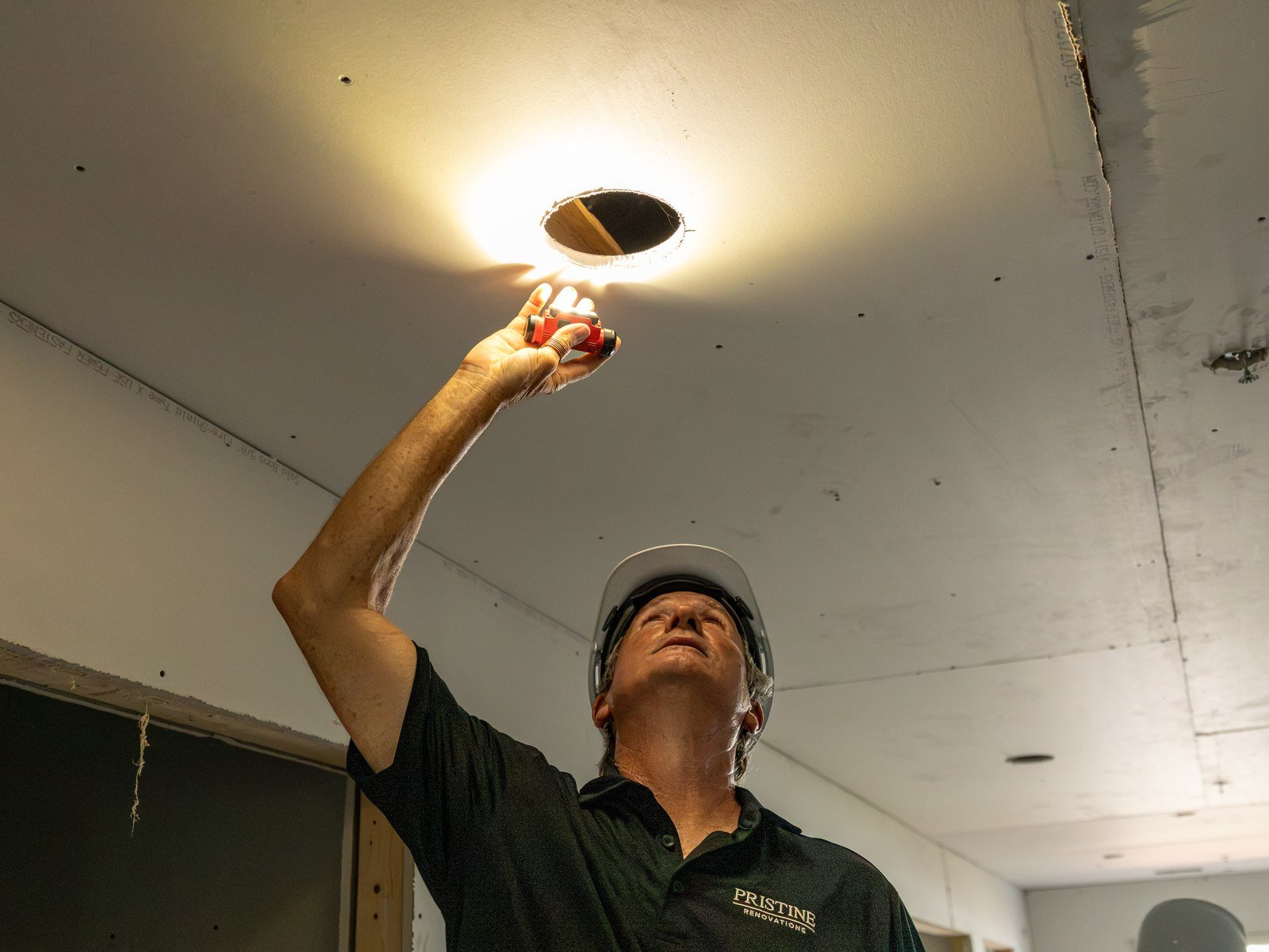 Pristine crew member checking a recessed ceiling light during renovation