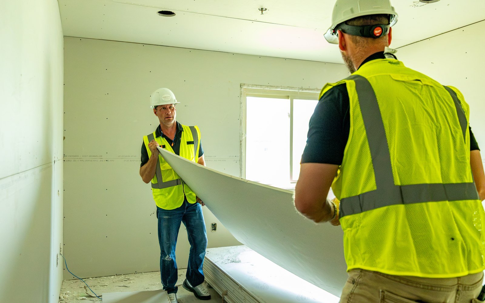 Two Pristine crew members carrying a sheet of drywall at a renovation site